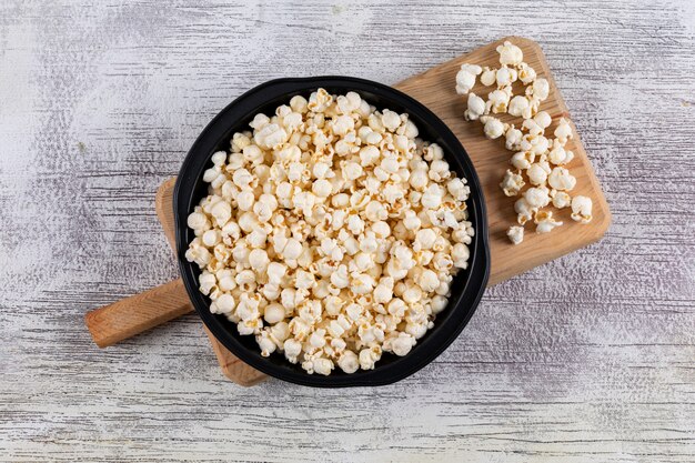 Top view of popcorn in black pan and cutting board on white wooden  horizontal