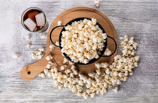 Top view of popcorn in black pan and wooden cutting board with lemonade on white surface horizontal