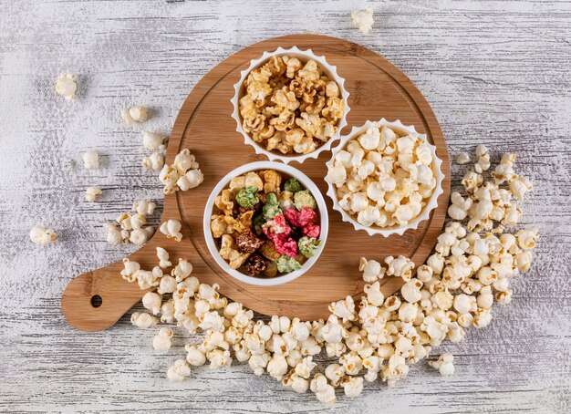 Vista superiore di popcorn in ciotole e tagliere di legno sull'orizzontale bianco