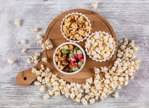 Top view of popcorn in bowls and wooden cutting board on white  horizontal