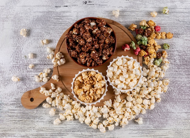 Top view of popcorn in bowls and wooden cutting board on white  horizontal