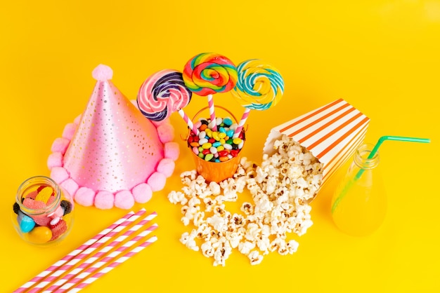 A top view popcorn and candies along with pink funny cap and cocktail