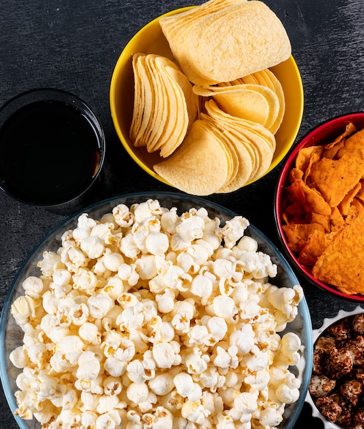 Top view of popcorn and chips in bowls on black  horizontal