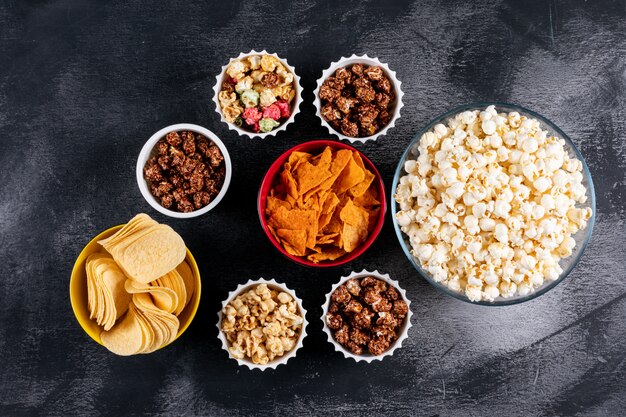 Top view of popcorn and chips in bowls on black  horizontal