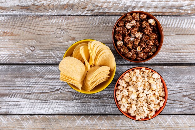 Top view of popcorn and chips in bowls on white wooden  horizontal