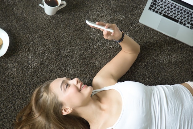 Top view portrait of woman lying on carpet, phone in hand