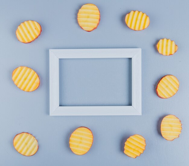 Top view of potato slices around frame on blue surface with copy space