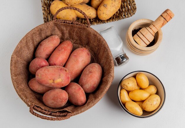 Top view of potatoes in basket and in plate with salt black pepper on white