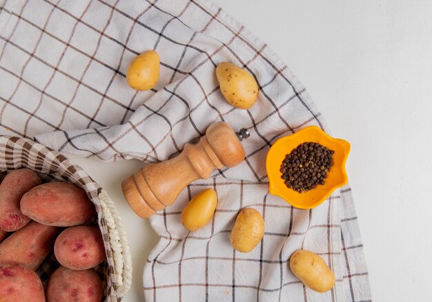 Top view of potatoes in basket with other ones salt black pepper on cloth on white