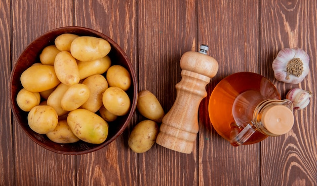 Top view of potatoes in bowl with garlic salt and butter on wooden surface