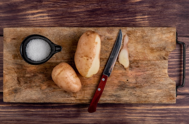 Top view of potatoes salt knife on cutting board on wood