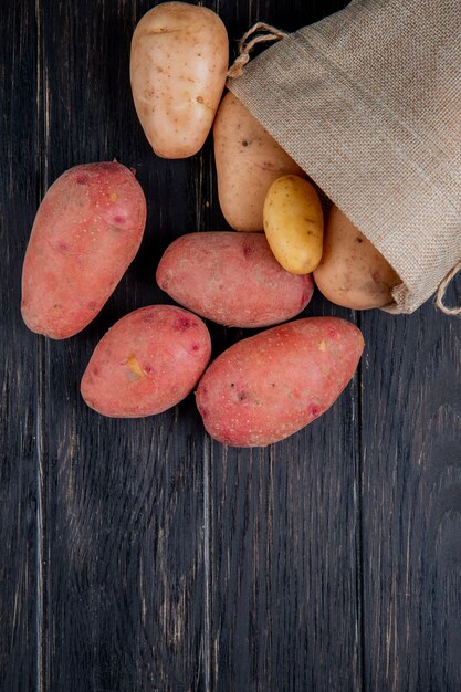 Top view of potatoes spilling out of sack on wood with copy space