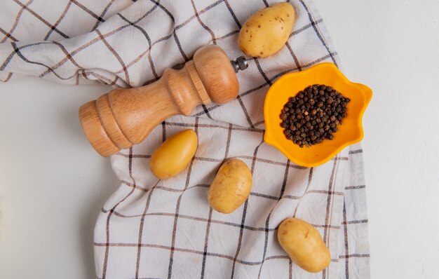 Top view of potatoes with salt and black pepper seeds on plaid cloth on white