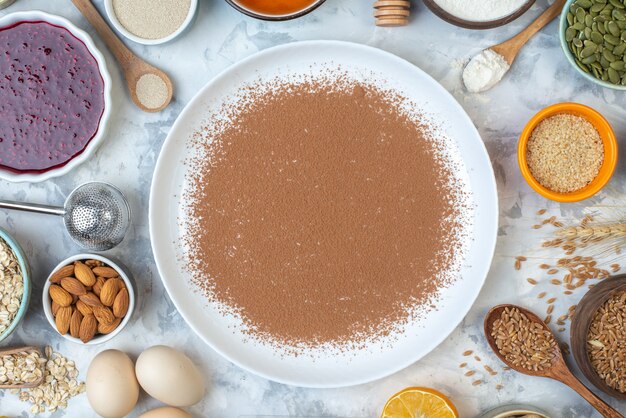 Top view powdered cacao on round plate bowls with jam almonds oats sesame seeds wheat grains eggs on table