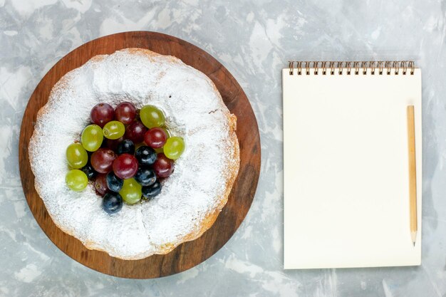 흰색 책상에 신선한 포도와 메모장을 넣은 탑 뷰 가루 케이크 맛있는 구운 케이크