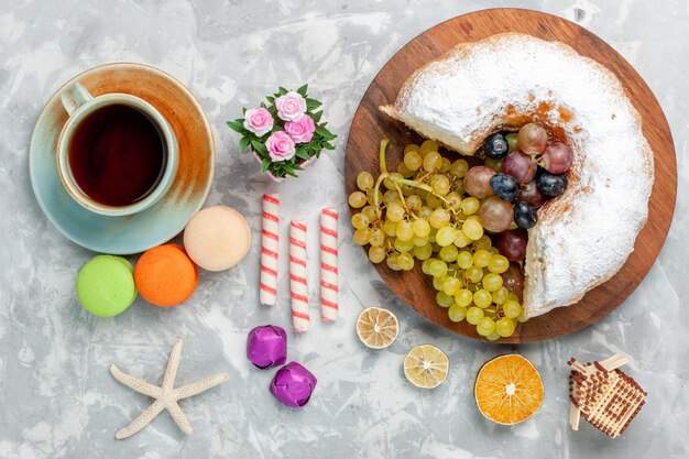 白い机の上に新鮮なブドウのお茶とフランスのマカロンとトップビューの粉末ケーキ