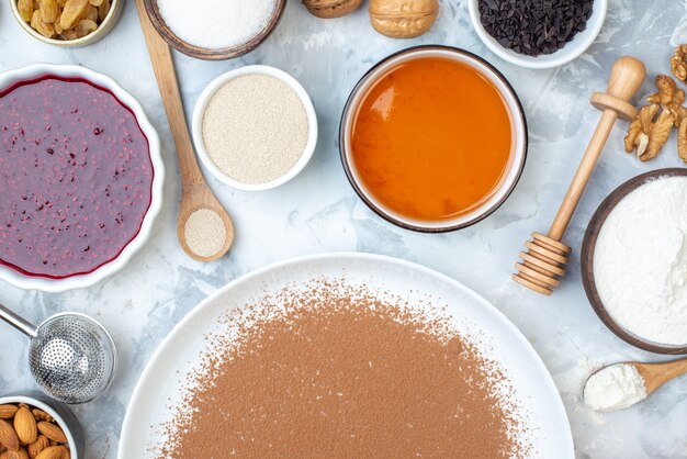 Top view powdered cocoa on round plate walnut bowls with jam honey flour wooden spoon honey stick on table