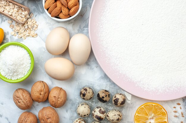 Top view powdered flour on plate bowls with flour and almonds walnut quail eggs oats on table