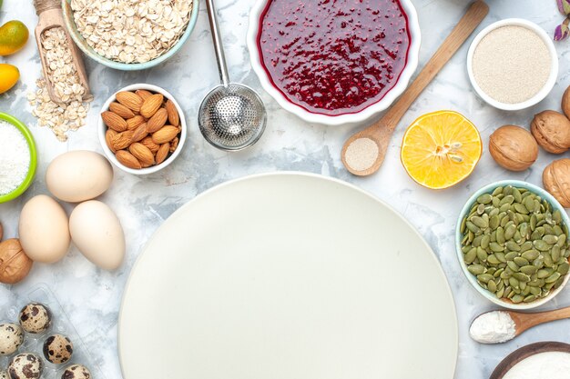 Top view powdered flour on plate bowls with oats squash seeds seeds almonds jam peanuts eggs quail eggs walnuts