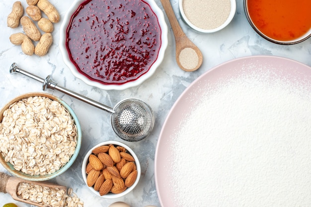 Top view powdered flour on plate bowls with sesame seeds oats almonds jam peanuts wooden spoon on table