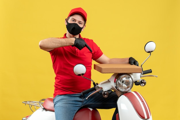 Top view of proud confident courier man wearing red blouse and hat gloves in medical mask sitting on scooter showing order
