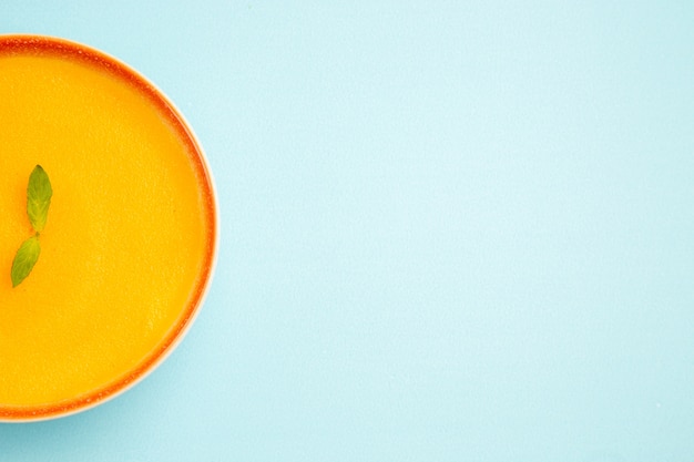 Top view of pumpkin soup inside plate on a blue background