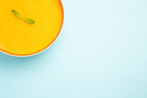 Top view of pumpkin soup inside plate on blue floor