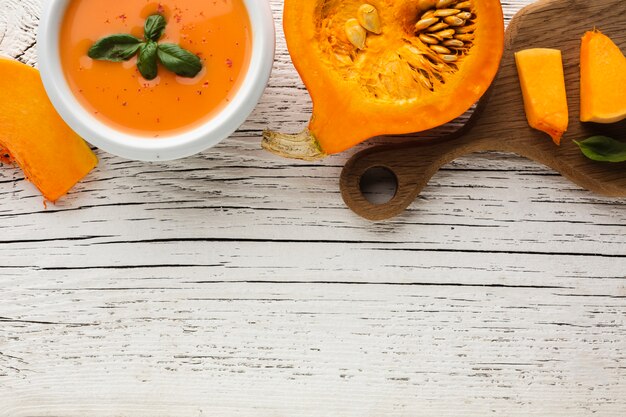 Top view pumpkin soup and pumpkin on cutting board with copy space