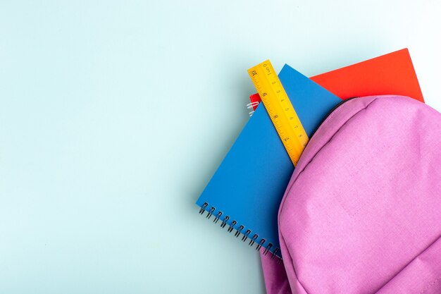 Top view purple bag with copybooks on the blue surface