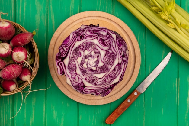 Free photo top view of purple cabbage on a wooden kitchen board with knife with radishes on a bucket with celery isolated on a green wooden wall