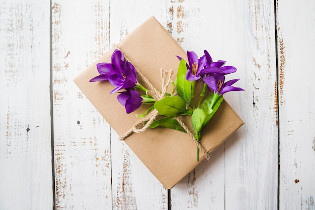Top view of purple flowers tied with gift box on white wooden backdrop