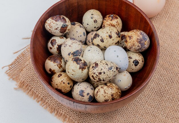 Top view of quail eggs with cream-colored shell on a brown bowl on sack cloth on white background
