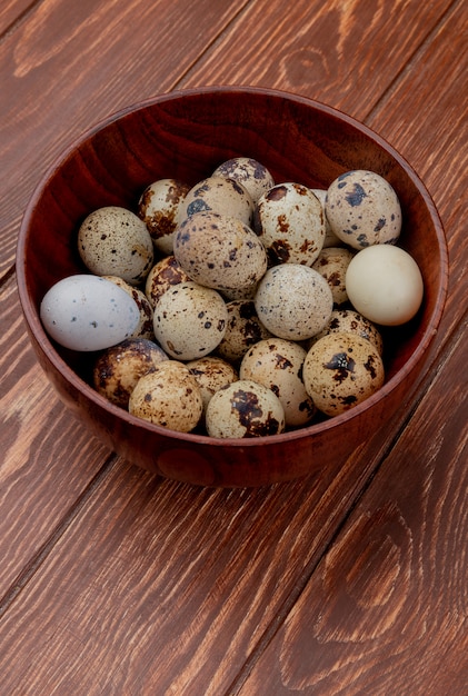 Вид сверху перепелиных яиц с кремовой скорлупой на деревянной миске на деревянном фоне