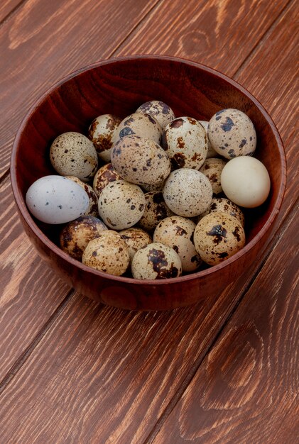 Top view of quail eggs with cream colored shells on a wooden bowl on a wooden background