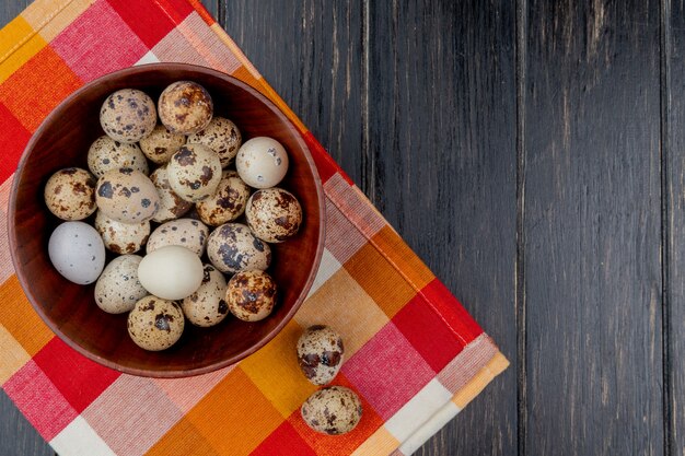 Free photo top view of quail eggs on a wooden bowl on checked tablecloth on wooden background with copy space