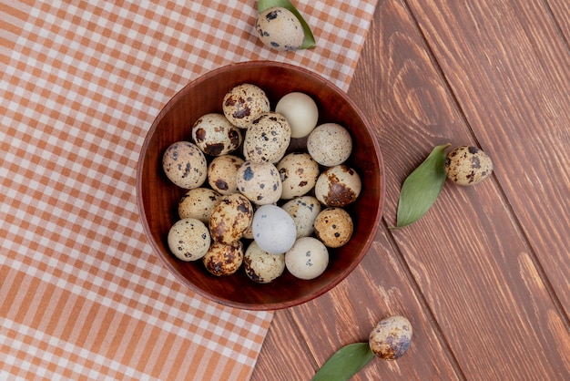 Top view of quail eggs on a wooden bowl on checked tablecloth on a wooden background