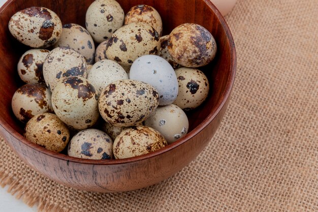 Top view of quail eggs on a wooden bowl on sack cloth background