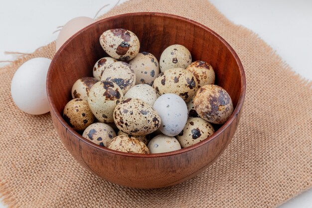 Top view of quail eggs on a wooden bowl on sack cloth on white background