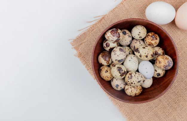 Вид сверху перепелиных яиц на деревянной миске на мешковине с куриными яйцами на белом фоне