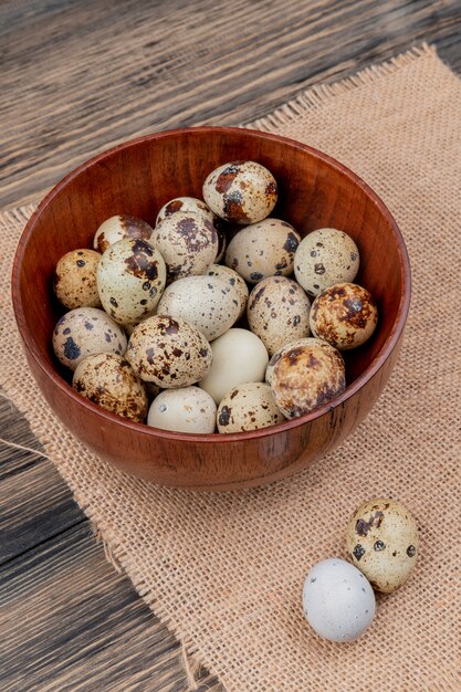 Top view of quail eggs on a wooden bowl on a sack cloth on a wooden background