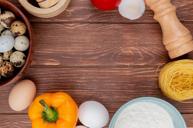 Top view of quail eggs on a wooden bowl with chicken egg with yellow bell pepper on a wooden background with copy space