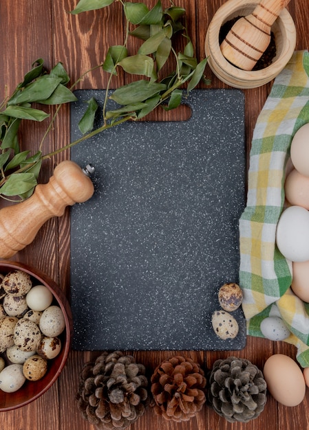 Vista superiore delle uova di quaglie su una ciotola di legno con le foglie con le pigne su un fondo di legno con lo spazio della copia