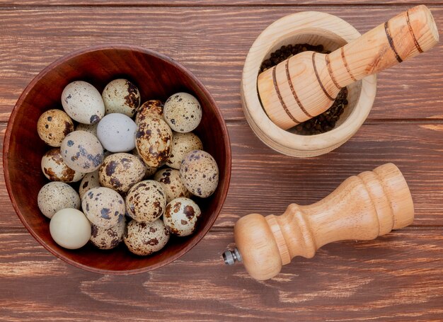 Top view of quail eggs on a wooden bowl with mortar and pestle with salt shaker on a wooden background