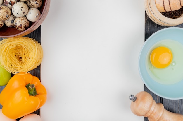 Top view of quail eggs on a wooden bowl with an orange bell pepper on a wooden background with copy space