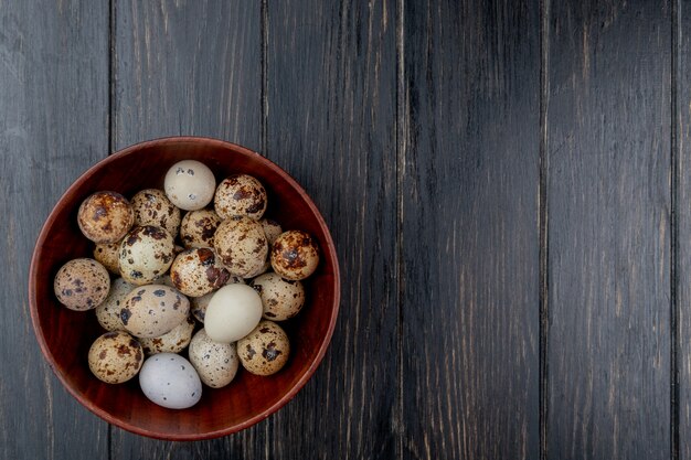 Top view of quail eggs on a wooden bowl on a wooden background with copy space