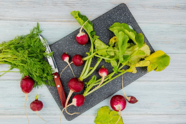 Free photo top view of radishes and knife on cutting board with bunch of dill on wooden background