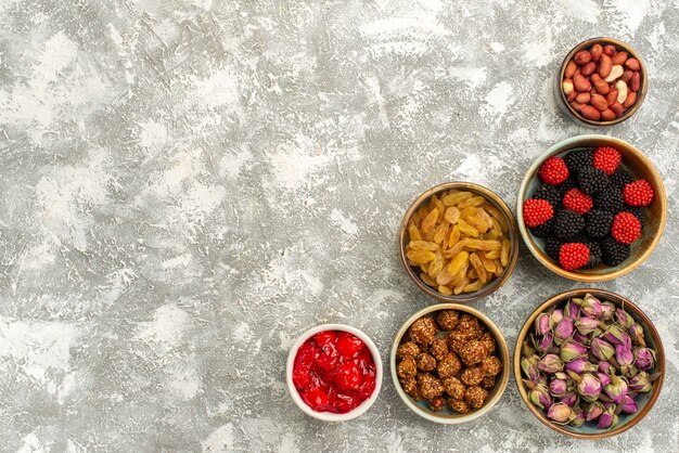 Вид сверху изюм и орехи с конфитюрами на белом фоне, конфеты, торт, чай, конфитюр, печенье