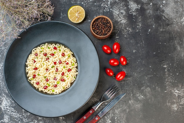 Top view ramen noodles on round plate red white checkered napkin a fork and knife on dark background