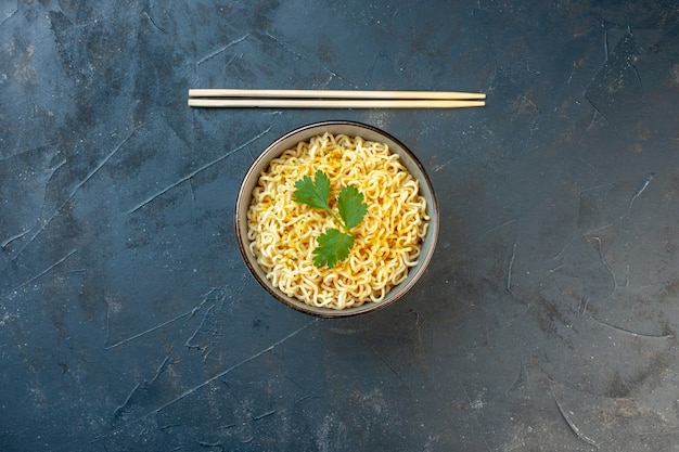 Top view ramen noodles with coriander in bowl chopsticks on dark table