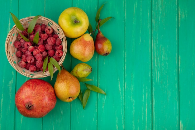 Top view of raspberries in basket with pomegranate peach and apple on green surface